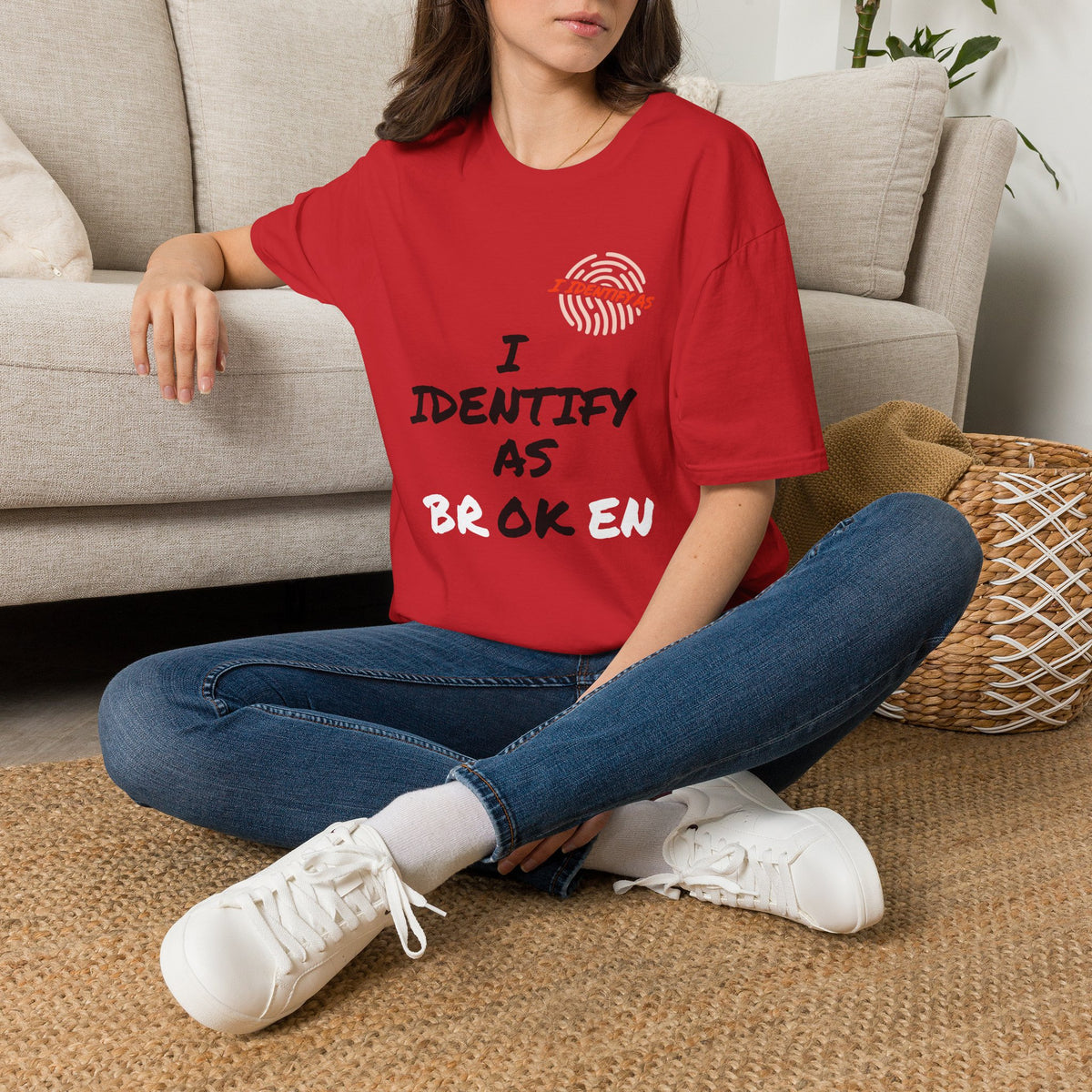 Person wearing a red t-shirt with a colorful phoenix design, sitting on the floor in a living room. T‑shirt with “I Identify As Broken / OK” dual‑meaning slogan designed in Dartford, UK.