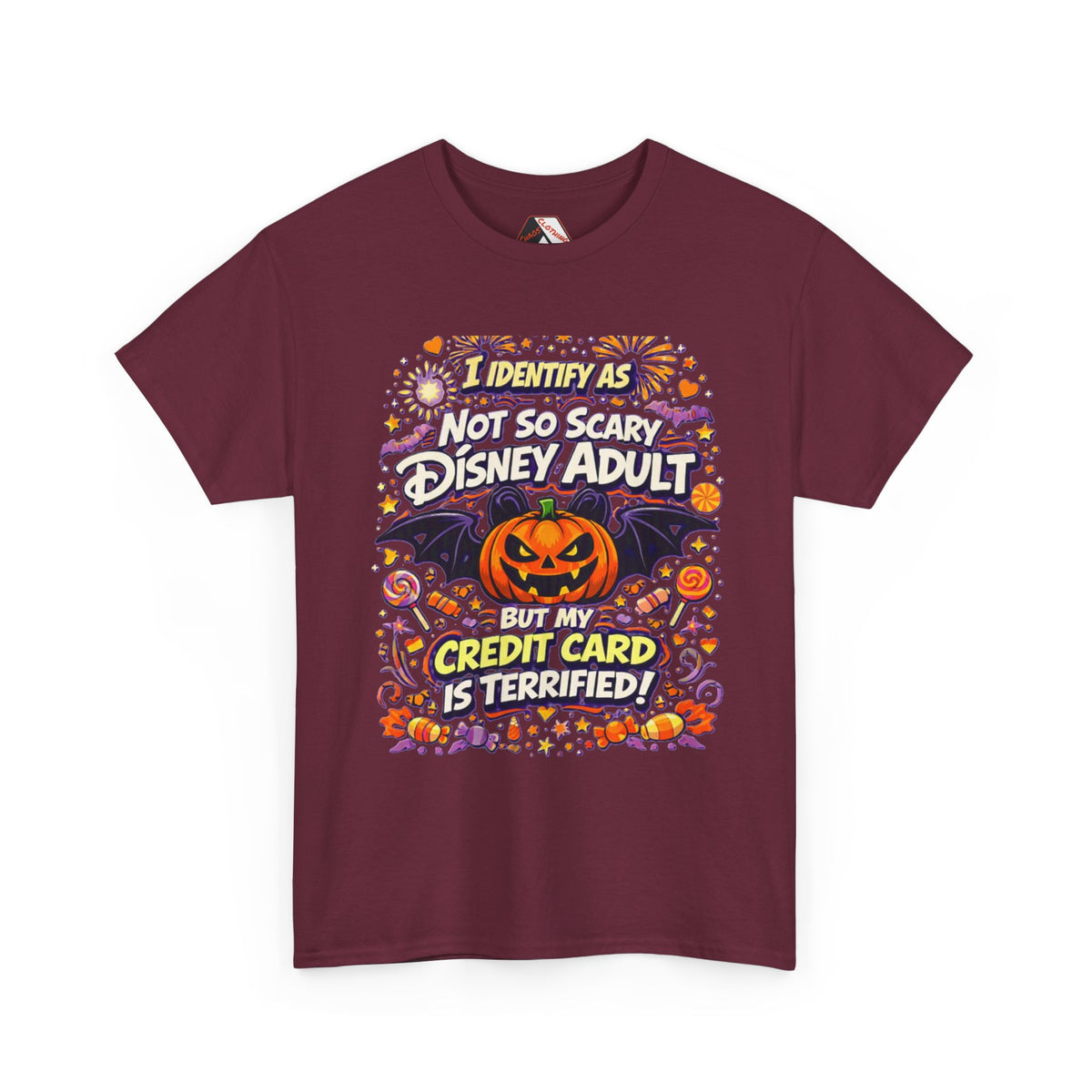 A Maroon short-sleeve crewneck t-shirt with a colorful graphic print on the front. The graphic features a jack-o'-lantern, bats, candy corn, and fireworks, with the text 'I IDENTIFY AS NOT SO SCARY DISNEY ADULT BUT MY CREDIT CARD IS TERRIFIED!' in stylized fonts.