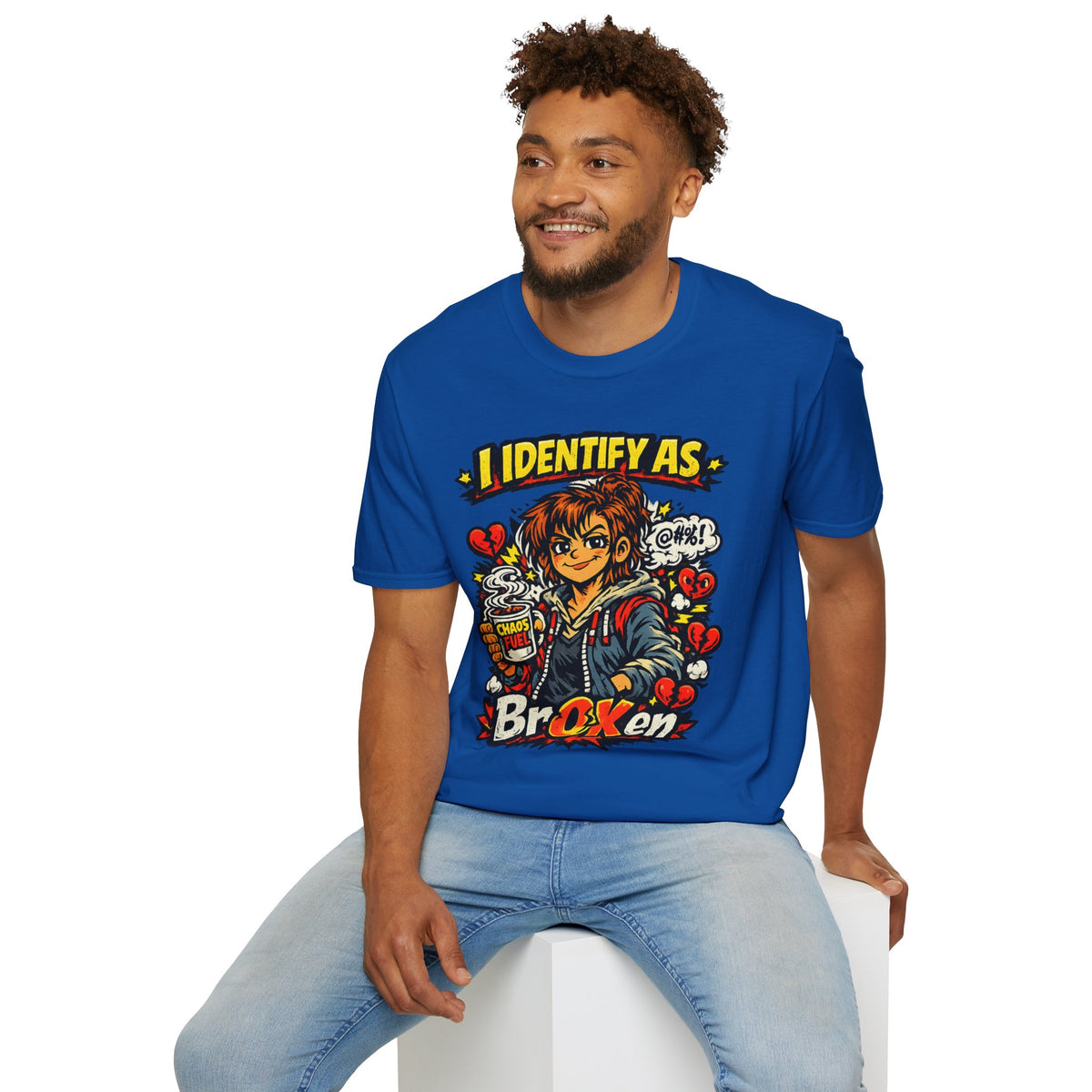 A man wearing a royal blue graphic t-shirt and light wash jeans, sitting on a white block against a plain white background. The t-shirt features a colorful anime-style graphic of a character with the text 'I IDENTIFY AS BROKEN' from Chaos Clothing by I Identify As