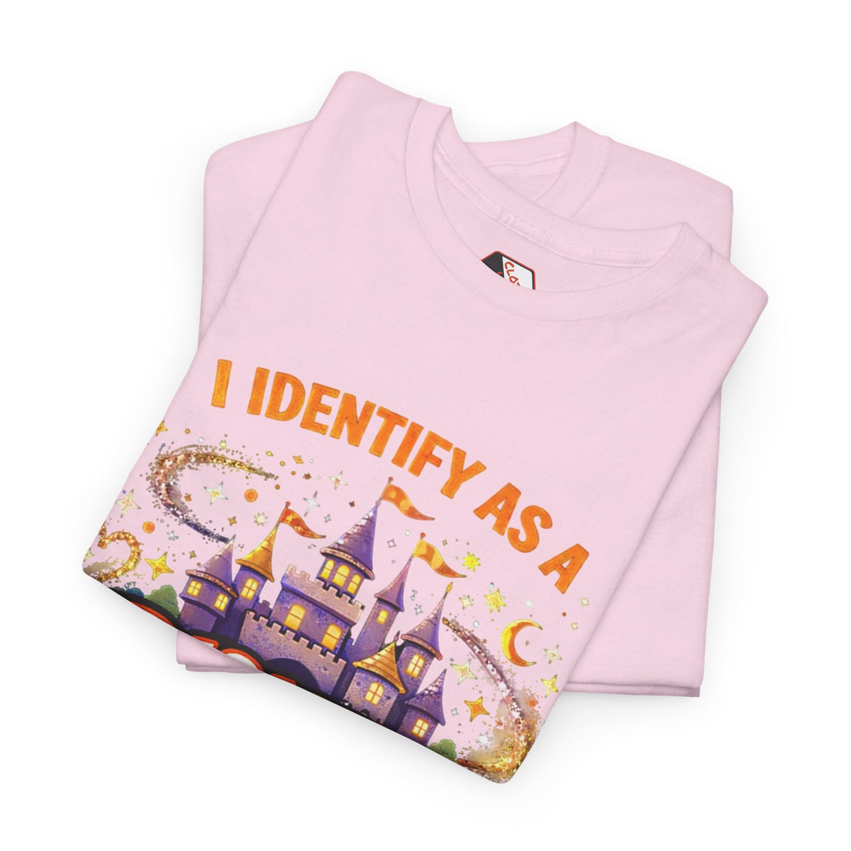 A folded light pink t-shirt with a graphic print of a purple castle, stars, and the text 'I IDENTIFY AS A' in orange, displayed on a clean white background.